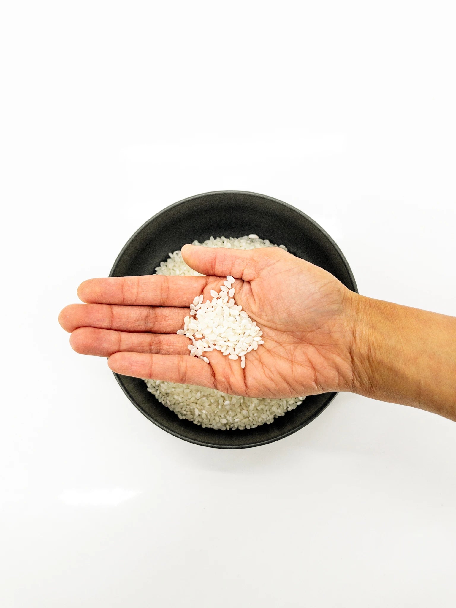 Main tenant des grains de riz japonais secs au dessus d'un bol noir contenant d'autres grains de riz secs | Eat in Japan épicerie en ligne